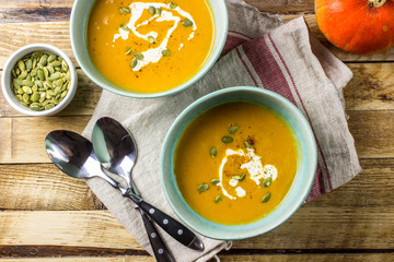 Roasted pumpkin and carrot soup with cream and pumpkin seeds on wooden background. Top view. Copy space