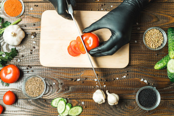 women's hands cut a tomato, next to lie the paprika, herbs, cucumbers and seasonings