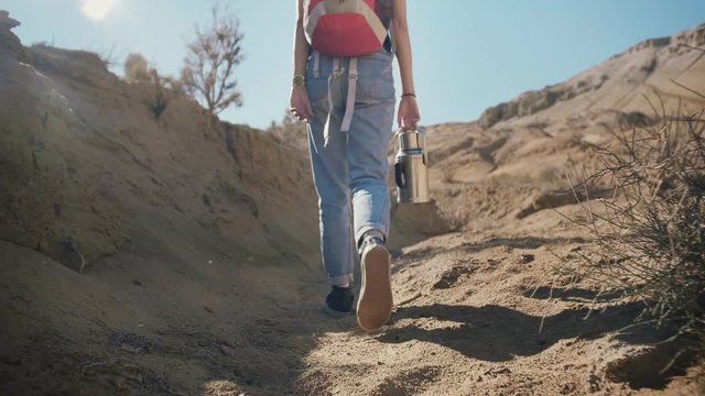Brave millennial traveler hipster female walking alone with water in thermos in middle of endless hot desert next mountains rock with beautiful view of blue sky in vacations holidays travel to Nature