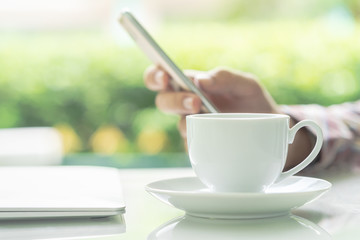 Male hands holding smart phone and cup of coffee on the table