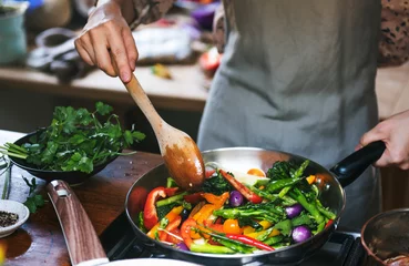Foto op Plexiglas Koken Vrouw kookt roergebakken groenten