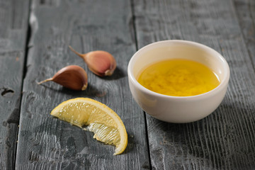 Olive oil with garlic and lemon in a white bowl on a dark table. Dressing for diet salad.