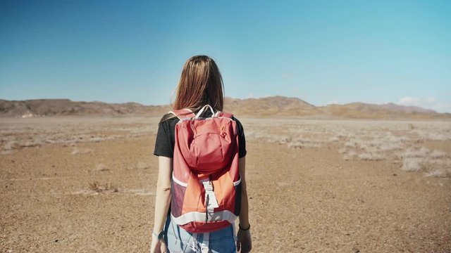 Millennial traveler hipster female with backback walking in middle of hot endless desert to infinity alone enjoying beautiful view of blue sky in vacations or holidays travel to Nature in loneliness
