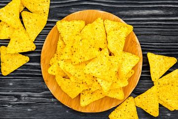 Mexican snack. Make nachos. Crispy nachos on wooden cutting board on black wooden background top view