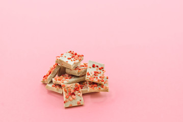 Chocolate bar pieces with dried strawberry on a pink abstract background.