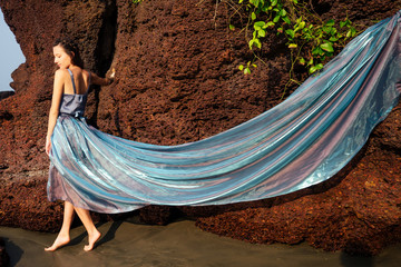 Young beautiful caucasian mermaid woman in long tull dress on coast of sea .Tropical photo of a charming girl in a chic outfit