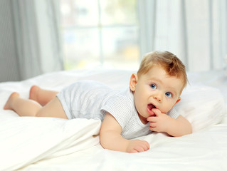 Charming blue-eyed baby 10 months in bed in a striped jumpsuit