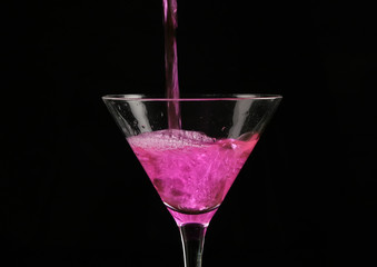 pink cocktail poured into a glass on a dark background.