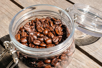 Close up dark brown roasted coffee beans in a glass jar in daylight 