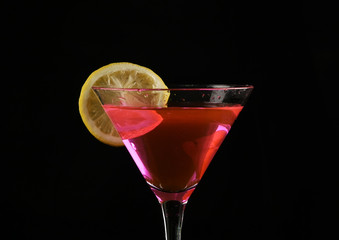 piece of lemon is thrown into a glass with pink cocktail on a dark background