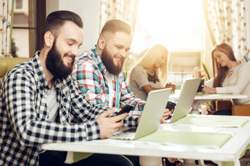 Two men sitting in a cafe look at mobile phones