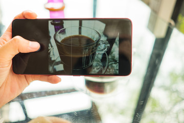 technology background hand of woman using mobile phone take photo coffee cup in restaurant