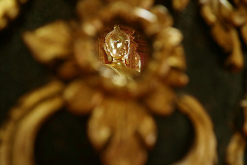 Closed Up the Face of Golden Buddha Image Reflecting on the Mirror of Teak Lacquered Pillar in Wat Phumin Temple, Nan Province, Thailand 
