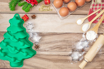 Christmas baking cake background. Ingredients and tools for baking - flour, eggs, silicone molds in the shape of a Christmas tree, and a rolling pin on a wooden background. With free text space.
