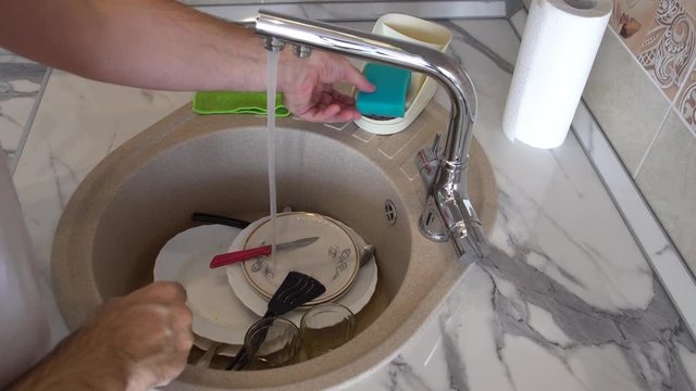 Man carefully washes dishes in the kitchen