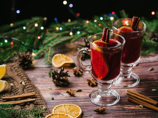 mulled wine in glass glasses with orange, cinnamon, cardamom, a anise stars on the table decorated with a Christmas tree and a garland. Traditional hot new year's eve alcoholic drink