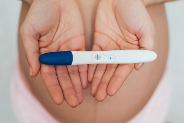Obraz na płótnie Canvas positive pregnancy test in the hands of a pregnant girl on the background of the abdomen