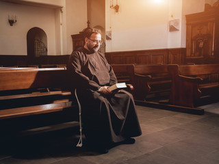 A monk in robes with holy bible in their hands praying in the church