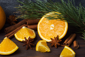 Christmas concept with cinnamon, fresh oranges and fir branches on a dark background with copy space.