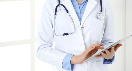 Woman doctor using tablet computer while standing straight in hospital closeup. Healthcare, insurance and medicine concept