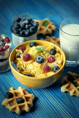 Tasty cornflakes with raspberries and blueberries on blue background. Wafers and milk.