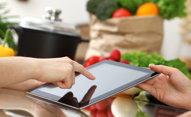 Close-up of human hands using tablet or touch pad. Two women in kitchen. Cooking, friendship or online shopping concepts