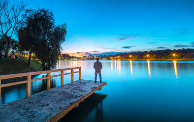 Da Lat, Vietnam - October 29th, 2018: Man standing on a small bridge reflecting on the lake at sunrise as a relaxing way to welcome the beautiful new day