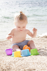 Cute baby playing with plastic toys on the pebble beach near the sea