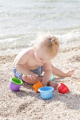 Cute baby playing with plastic toys on the pebble beach near the sea