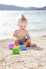 Cute baby playing with plastic toys on the pebble beach near the sea