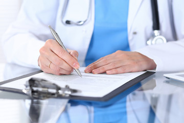 Female doctor filling up medical form on a clipboard, closeup. Healthcare, insurance and medicine concept