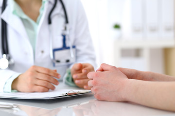 Doctor and patient talking while sitting at the desk in hospital office, close-up of human hands. Medicine and health care concept