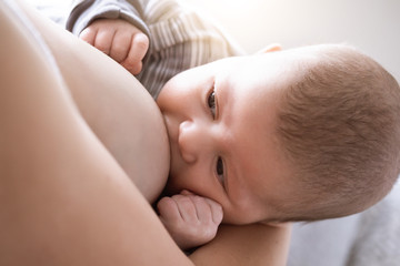 Close-up of mother breastfeeding and hugging newborn baby. Mom breast feeding her infant baby. Lactation newborn concept. Baby eating milk before sleeping. Mother feed her month son with breast milk
