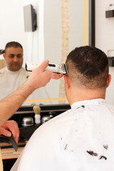 Fototapeta premium Back view of man getting short hair trimming at barber shop with clipper machine