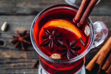 Mulled red wine with spices and orange in glass on a wooden rustic background.