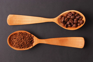 instant coffee in a wooden spoon and coffee beans on a wooden background.