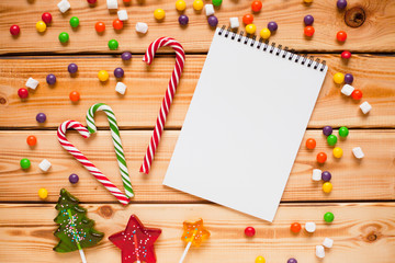 Open notebook with blank pages and colorful lollipops on the wooden background. Flat lay, top view. Christmas planning and New Year concept, holiday decorations 2019 Goals.