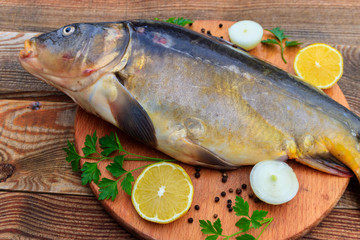 Raw carp fish with lemon, onion, pepper and parsley on cutting board on rustic wooden table