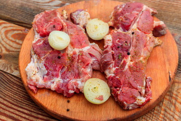 Fresh raw pork meat with spices and onion on wooden cutting board on rustic table