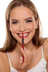 young beautiful and happy girl shaping her lips with lip pencil on white backgeound