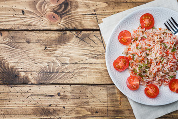 Rice with tomato sauce and greens on wooden background. Copy space
