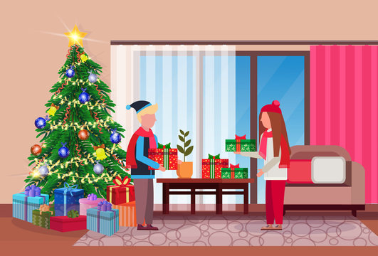 merry christmas happy new year couple give each other present gift box in living room pine tree home interior decoration winter holiday concept flat horizontal