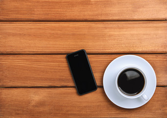 A cup of hot coffee and mobile phone on a dark wooden background. Copy space, top view, flat lay