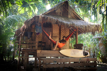 surfer in hammock at tropical  beach cottage with palm trees and surfboard