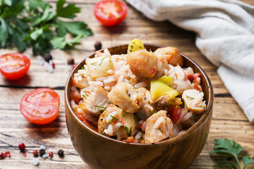Stewed rice with chicken and vegetables in a wooden bowl.