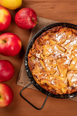 A closeup photo of an apple pie in a pan, shot from above on a dark rustic wooden background with apples and a place for text