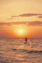 Silhouette of man on a SUP board in sea at sunset.