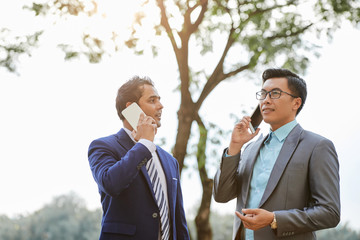 Two business consultants in suits discussing something on mobile phone while standing outdoors