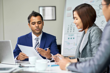 Male leader sitting at the table and discussing some document with his colleagues during a meeting