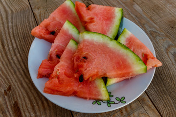 Fresh ripe sliced watermelon in white plate on rustic wooden table
